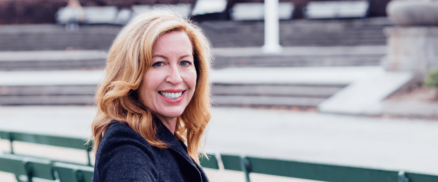 Portrait of a woman smiling outdoors with a park bench in the background.