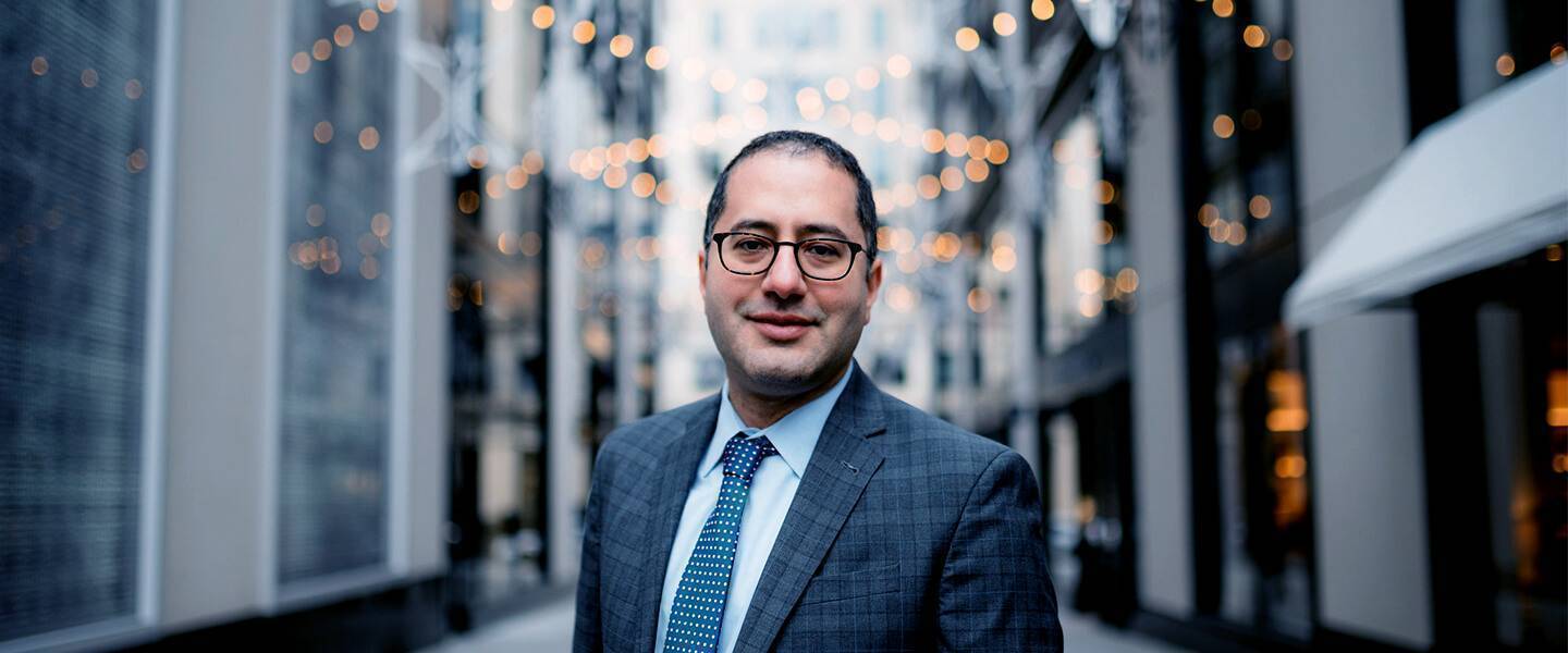 Chris Khoury smiling in a professional setting with modern buildings and lights in the background.